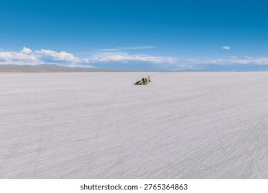 This captivating image captures the vast expanse of the Salar de Uyuni in Bolivia, the world's largest salt flat, under a stunning blue sky dotted with scattered clouds. The seemingly endless white surface stretches towards the horizon, creating a surreal and otherworldly landscape. In the distance, faint outlines of mountains add depth to the scene. A construction vehicle sits in the middle of the image, adding an element of human presence to the otherwise untouched terrain. The bright, reflective surface amplifies the natural light, creating a sense of openness and tranquility. The immense scale of the salt flat emphasizes the feeling of solitude and isolation, while the clear sky and crisp air evoke a sense of adventure and exploration. The interplay between the pristine white salt, the azure sky, and the distant mountains creates a visually striking and unforgettable scene in Bolivia. The image encapsulates the unique beauty and natural wonders of this South American country.