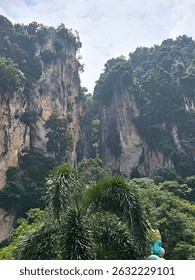 This captivating image features towering limestone cliffs enveloped in dense greenery, showcasing nature's grandeur. The vibrant flora offers a rich contrast against the rugged rock formations.