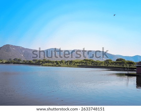 This captivating image showcases the tranquil beauty of Man Sagar Lake in Jaipur, Rajasthan, India, framed by the majestic Aravalli Hills under a clear blue sky. The serene waters of the lake reflect 