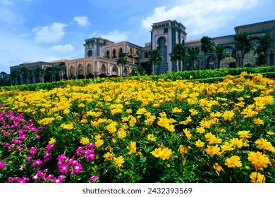 This captivating image showcases a vibrant garden of yellow and pink flowers in front of an elegant building. The building features arches, columns, and towers, displaying architectural finesse.