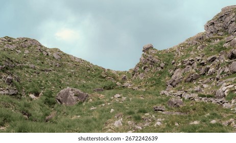 This captures a view looking up through the Gap of Dunloe. The rocky terrain is covered with green grass, creating a rugged landscape. It is located in County Kerry, Ireland.