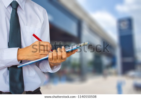 This career man saleman\
business inspection writing note on notepad or \book, paper with\
showroom  blurry background.for transport automobile \automotive\
image.