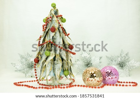 This Christmas tree is made of dried fish. Near the tree are traditional Christmas decorations - balls made of pieces of mirrors. The background is decorated with Christmas snow-silver flowers.
