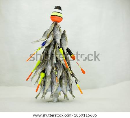 This Christmas tree is made of dried fish. New year for the fisherman. The tree is decorated with floats and fishing tackle. The background is decorated with Christmas snow-silver flowers.