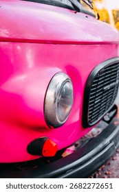 This close view captures a bright pink vintage car with its distinctive rounded headlight and elegant grille.