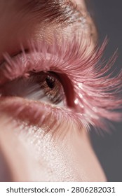This close view features a woman's eye with striking pink eyelashes that add a unique flair, showcasing her natural beauty under soft lighting