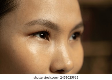 This close-up captures the detailed facial features of an Asian woman, highlighting her expressive eyes, skin texture, and natural beauty. Her gaze holds a story, reflecting her thoughts or emotions - Powered by Shutterstock