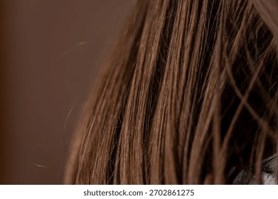 This close-up image features long brown hair showcasing soft highlights and gentle waves against a warm neutral background, emphasizing a natural beauty with a