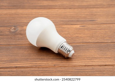 This is a close-up image of an LED light bulb lying on a wooden surface. - Powered by Shutterstock