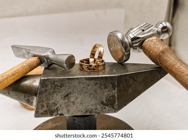 This close-up image showcases two handmade, hammered metal rings resting on an anvil, surrounded by jeweler's hammers. Perfect for promoting custom jewelry, craftsmanship, or jewelry-making workshops. - Powered by Shutterstock