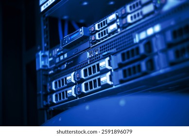 This close-up image shows a server rack illuminated by blue lighting, showcasing various hardware components and cables, representing modern technology infrastructure.