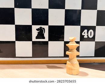 This is a close-up, low-angle shot of a set of light-colored wooden chess pieces lined up on a wooden surface.

In the foreground, the are in sharp focus - you can see the natural wood grain and signs of wear and age. Some chipped and damaged, most noticeably the knight piece in the center which has a broken nose and a large chip on its side. The tallest pieces, the king and queen, stand in the middle of the row, flanked by pawns and other pieces.