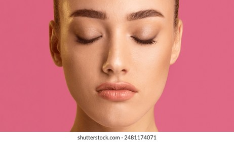 This is a close-up photo of a woman face with her eyes closed. The photo is taken against a pink background, and the focus is on the woman eyes, nose, and mouth. - Powered by Shutterstock