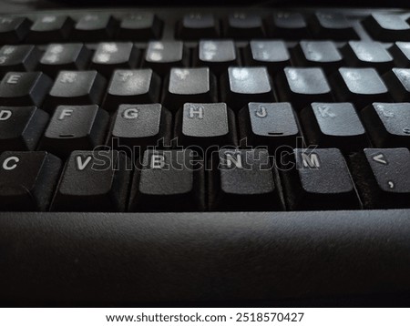 This close-up shot of a computer keyboard highlights the textured surface of the keys and the subtle interplay of light and shadow. The dark color scheme creates a sense of sophistication and mystery,