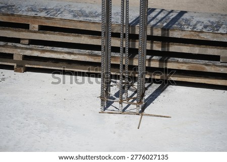 This close-up view shows the base of a steel rebar column emerging from a freshly poured concrete slab on a sunny construction site, highlighting foundational work.