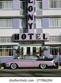 This is the Colony Hotel on the strip of South Beach Miami. There is a purple and black vintage car parked in front of the hotel.