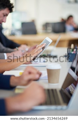 This company is cutting edge. Cropped shot of a group of business professionals sitting around the table in a meeting while using modern technology.