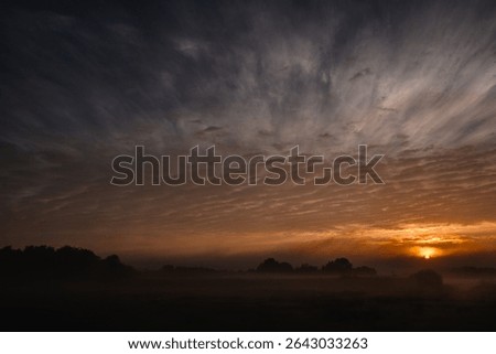 This compelling image showcases the intense and brooding beauty of twilight. The dark, expansive sky is streaked with dramatic cloud formations, while the setting sun provides a fiery focal point