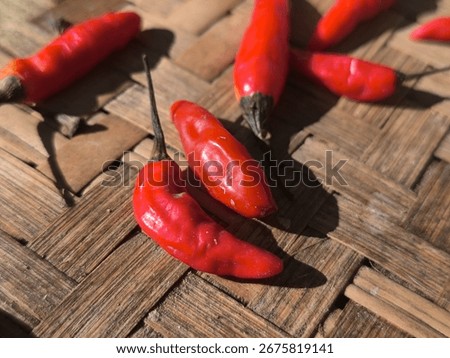 This composition captures a pair of richly colored red chili peppers, one slightly wrinkled, the other smooth, set on the textured bamboo surface. The sunlight casts soft, elongated shadows, adding a 
