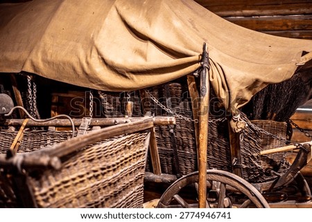 This comprehensive collection of high-quality documentary photographs captures the authentic atmosphere of historical rural life within the Wallachian Open Air Museum in Roznov pod Radhostem, Czech Republic. The images offer a detailed look into the interior of a traditional timber-framed barn and workshop, showcasing an extensive array of antique agricultural machinery and handcrafted wooden tools used by ancestors in the Moravian Wallachia region.The focus lies on the intricate craftsmanship of vintage wooden horse-drawn wagons, carts, and carriages, featuring weathered spoked wheels, iron-forged reinforcements, and hand-woven wicker baskets used for transporting goods. Each frame highlights the rustic texture of aged wood, the patina of time-worn metal components, and the dusty, atmospheric lighting of the museum's interior. Notable details include a heavy wooden mallet, disassembled wheel parts, and various farming implements stored in a dimly lit, hay-filled environment. These photographs serve as a visual archive of European folk architecture, traditional carpentry, and the pre-industrial era of farming, reflecting the hard-working spirit and ingenuity of 19th-century rural society. The composition emphasizes the play of light and shadow on organic materials, making it ideal for historical documentaries, educational materials, and heritage preservation projects.