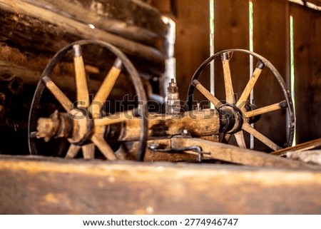 This comprehensive collection of high-quality documentary photographs captures the authentic atmosphere of historical rural life within the Wallachian Open Air Museum in Roznov pod Radhostem, Czech Republic. The images offer a detailed look into the interior of a traditional timber-framed barn and workshop, showcasing an extensive array of antique agricultural machinery and handcrafted wooden tools used by ancestors in the Moravian Wallachia region.The focus lies on the intricate craftsmanship of vintage wooden horse-drawn wagons, carts, and carriages, featuring weathered spoked wheels, iron-forged reinforcements, and hand-woven wicker baskets used for transporting goods. Each frame highlights the rustic texture of aged wood, the patina of time-worn metal components, and the dusty, atmospheric lighting of the museum's interior. Notable details include a heavy wooden mallet, disassembled wheel parts, and various farming implements stored in a dimly lit, hay-filled environment. These photographs serve as a visual archive of European folk architecture, traditional carpentry, and the pre-industrial era of farming, reflecting the hard-working spirit and ingenuity of 19th-century rural society. The composition emphasizes the play of light and shadow on organic materials, making it ideal for historical documentaries, educational materials, and heritage preservation projects.