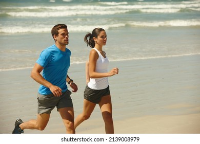 This Couple Takes Being Fit Serious. Shot Of A Young Couple Jogging Together On The Beach.