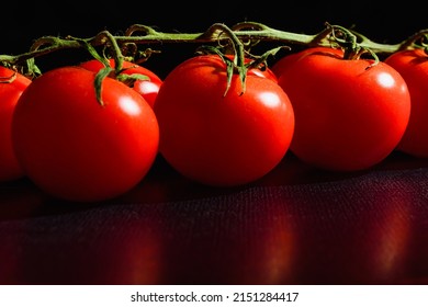 This Is Dark Food Photography Of Branch Of Cherry Tomatoes On Black Wooden Table. This Is Close Up View Of Red Tomato.