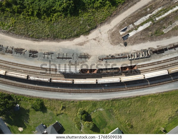 This is a drone photograph\
of an idle train on railroad tracks. Train cars and scattered metal\
are also visible along the sides, which adds more detail to the\
image.
