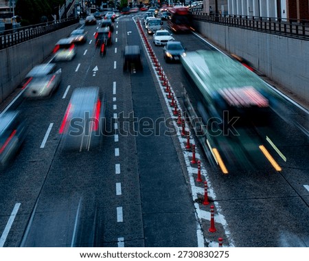 This dynamic photograph emphasizes the speed of urban transit, featuring a bus blurred into a green and white streak as it passes through the frame. The high-angle perspective and slow shutter speed highlight the contrast between the static concrete walls of the underpass and the energetic, fleeting movement of the vehicles within it.
