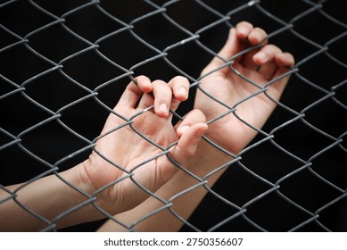 This evocative image captures hands gripping a metal fence, symbolizing struggle and confinement. The emotional tension reflects themes of vulnerability and hope.