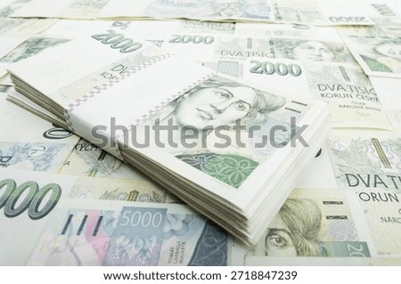 This eye-level, close-up shot captures a stack of Czech Koruna 2000 banknotes, neatly bound with a white label, resting atop a scattered array of various CZK bills, Czech Republic.