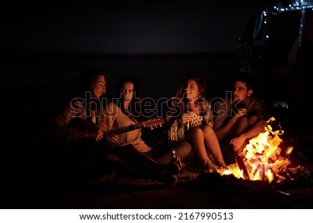 This is the feeling of freedom. Shot of a group of friends sitting around a bonfire on the beach at night.