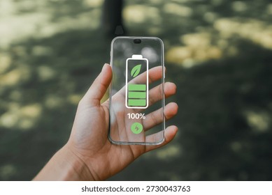 This forward-thinking image features a hand holding a transparent smartphone, displaying a vivid green battery icon at 100% capacity with a superimposed leaf. This symbolizes sustainable energy, eco-friendly technology, and environmental consciousness in the digital age. It represents concepts like green technology, renewable power, and the future of sustainable consumer electronics.