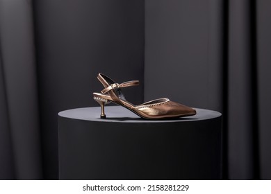 This is a golden colored heeled sandal, it has white stones on it, there are stones on the heel of the ski, there are sandals on the stool.