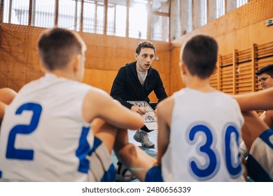 In this gym scene, kids attentively listen to their basketball coach, showing concentration in the sport environment - Powered by Shutterstock