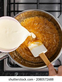 This Is The Hand Stirring The Caramel With The Added Cream Stirring Using A Spatula In A Saucepan On The Stove