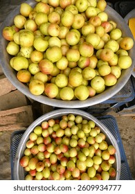 This high-angle shot captures two large, shallow metal bowls filled with fresh jujubes fruit commonly found in South Asia. The natural light highlights the textures and colors of the fresh produce.