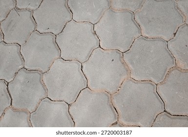 This high-angle shot features a textured surface of interlocking concrete pavement blocks. The blocks are shaped in a unique hexagonal or star-like pattern, creating a rhythmic geometric design across the frame. The weathered gray concrete shows fine sand and debris within the joints, suggesting an outdoor walkway or patio area. This image provides a clean, neutral background highlighting industrial masonry and architectural flooring patterns