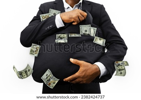 This high-impact conceptual image features a businessman in a sharp dark suit clutching a large black bag overflowing with United States one-hundred-dollar bills. Cash is seen bursting from the bag and tucked into his suit jacket, while several bills appear to float in the air, suggesting rapid wealth accumulation, greed, or a financial windfall. The focus is on the man's hands and the sheer volume of currency, set against a clean white background to emphasize the theme of success and profit.
