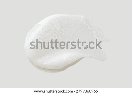 This high-quality image captures a pristine, thick smear of white cosmetic cream against a neutral, clean background. The visual emphasizes the luxurious and silky texture of the product, showcasing its rich consistency and smooth application. Such an image is essential for professional beauty branding, skincare marketing, and dermatological presentations. The smear features a delicate, whipped-like structure with subtle ridges that suggest a velvety feel upon touch. The light reflects softly off the surface, highlighting the creamy, non-greasy, and hydrating nature of the substance. The edges of the swatch are slightly irregular, providing an authentic 