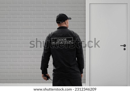 This high-quality image showcases a dedicated and professional door supervisor ensuring safety and security at a building entrance. The door supervisor, dressed in a distinctive security uniform.