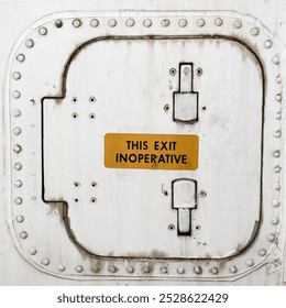 This high-resolution image features a close-up of an aircraft exit door with a prominently displayed 'THIS EXIT INOPERATIVE' sign. The weathered metal surface, complete with rivets and wear, offers a 
