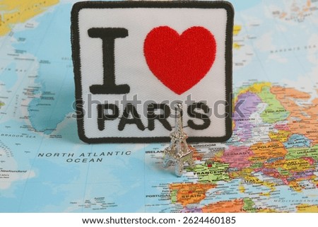 This horizontal photo features a small silver Eiffel Tower souvenir and embroidery art , placed on a map of Paris , symbolizing the charm and love travelers feel for France.
