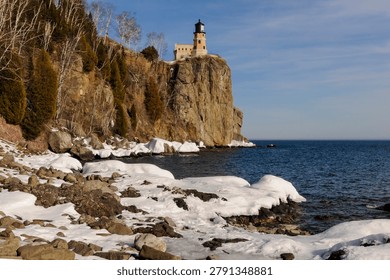 This is the iconic 1910 Split Rock Lighthouse on Lake Superior near Two Harbors, Minnesota in the middle of winter. A magnificent lighthouse completed in 1910 in a spectacular setting enhanced by lots of ice and white snow.  It was built to protect ships from the treacherous rocky coast after the devastating Mataafa Storm of 1905 that wreaked havoc and wrecked nearly 30 ships along Lake Superior's rocky coastline. There were no roads there at the time and 310 tons of materials were hoisted up the 133 foot sheer cliff from supply boats. The 133 foot shear cliff  the lighthouse sits on is most dramatic viewed from the lower lake shore area. Hiking here in winter can be a little treacherous with very large, rough rocks covered in thick ice and snow with the open lake waters right at the edge of the treacherous shore..