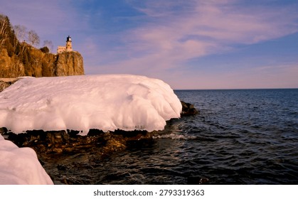 This is the iconic 1910 Split Rock Lighthouse on Lake Superior near Two Harbors, Minnesota in the middle of winter. A magnificent lighthouse completed in 1910 in a spectacular setting enhanced by lots of ice and white snow.  It was built to protect ships from the treacherous rocky coast after the devastating Mataafa Storm of 1905 that wrecked nearly 30 ships along Lake Superior's rocky coastline. There were no roads there at the time and 310 tons of materials were hoisted up the 133 foot sheer cliff from supply boats. The 133 foot shear cliff  the lighthouse sits on is most dramatic viewed from the lower lake shore area. Hiking here in winter can be a little treacherous with very large, rough rocks covered in thick ice and snow with the open lake waters right at the edge of the treacherous shore.