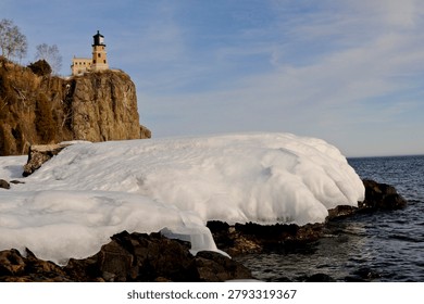 This is the iconic 1910 Split Rock Lighthouse on Lake Superior near Two Harbors, Minnesota in the middle of winter. A magnificent lighthouse completed in 1910 in a spectacular setting enhanced by lots of ice and white snow.  It was built to protect ships from the treacherous rocky coast after the devastating Mataafa Storm of 1905 that wrecked nearly 30 ships along Lake Superior's rocky coastline. There were no roads there at the time and 310 tons of materials were hoisted up the 133 foot sheer cliff from supply boats. The 133 foot shear cliff  the lighthouse sits on is most dramatic viewed from the lower lake shore area. Hiking here in winter can be a little treacherous with very large, rough rocks covered in thick ice and snow with the open lake waters right at the edge of the treacherous shore.