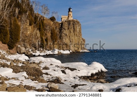This is the iconic 1910 Split Rock Lighthouse on Lake Superior near Two Harbors, Minnesota in the middle of winter. A magnificent lighthouse completed in 1910 in a spectacular setting enhanced by lots of ice and white snow.  It was built to protect ships from the treacherous rocky coast after the devastating Mataafa Storm of 1905 that wreaked havoc and wrecked nearly 30 ships along Lake Superior's rocky coastline. There were no roads there at the time and 310 tons of materials were hoisted up the 133 foot sheer cliff from supply boats. The 133 foot shear cliff  the lighthouse sits on is most dramatic viewed from the lower lake shore area. Hiking here in winter can be a little treacherous with very large, rough rocks covered in thick ice and snow with the open lake waters right at the edge of the treacherous shore..