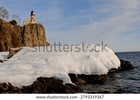 This is the iconic 1910 Split Rock Lighthouse on Lake Superior near Two Harbors, Minnesota in the middle of winter. A magnificent lighthouse completed in 1910 in a spectacular setting enhanced by lots of ice and white snow.  It was built to protect ships from the treacherous rocky coast after the devastating Mataafa Storm of 1905 that wrecked nearly 30 ships along Lake Superior's rocky coastline. There were no roads there at the time and 310 tons of materials were hoisted up the 133 foot sheer cliff from supply boats. The 133 foot shear cliff  the lighthouse sits on is most dramatic viewed from the lower lake shore area. Hiking here in winter can be a little treacherous with very large, rough rocks covered in thick ice and snow with the open lake waters right at the edge of the treacherous shore.