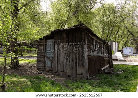 This is an image of an abandoned, rundown structure in a ghetto area, showcasing deteriorating wooden walls, rusted metal, and overgrown grass. The environment conveys neglect and decay.