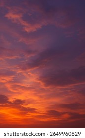 This image beautifully captures a sunset sky filled with vibrant and warm tones. The scene transitions from golden orange and fiery red near the horizon to deep purples and indigos at the top.